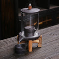 Glass cylinder purple clay backflow incense burner on natural wood stand with smoke waterfall