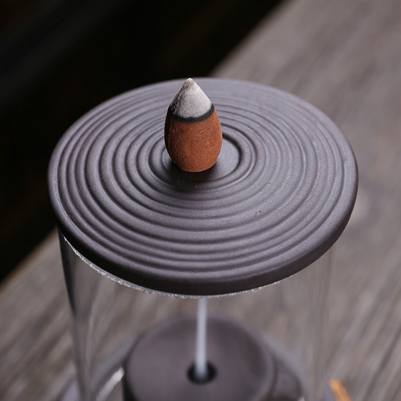 Backflow incense cone on concentric purple clay lid above clear glass chamber