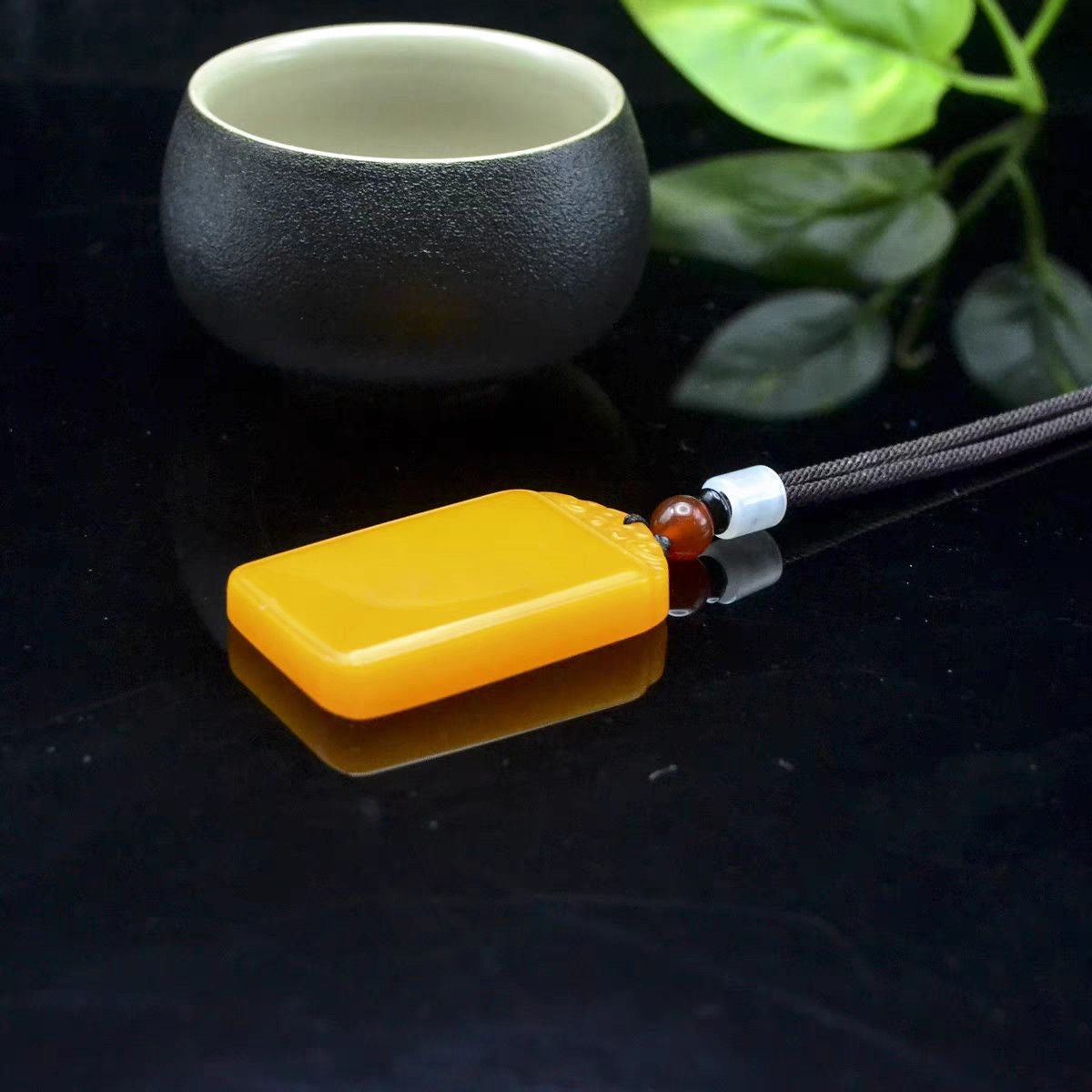 Golden yellow peace plaque pendant shown flat beside tea cup
