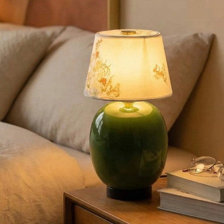 Green ceramic rechargeable bedside lamp glowing beside books and sofa