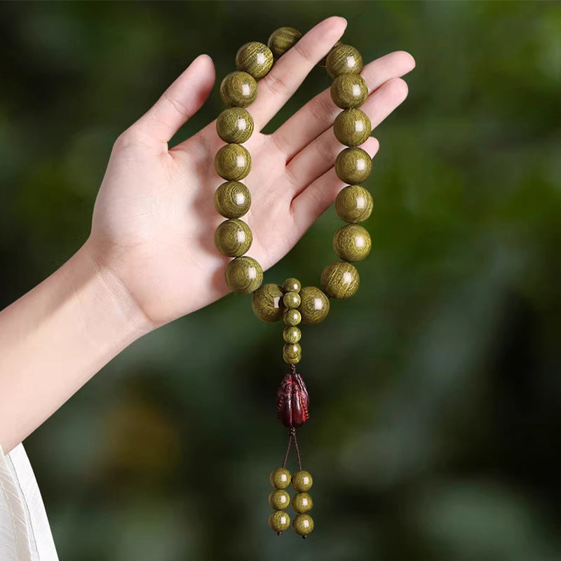 Green sandalwood-style 18mm hand mala held in hand with dark red carved focal bead and hanging bead tassel
