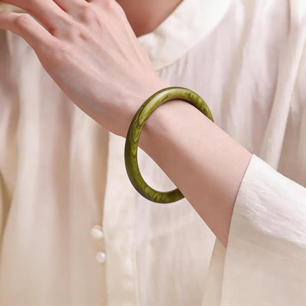 Green sandalwood-style round wood bangle bracelet worn on wrist with visible olive wood grain