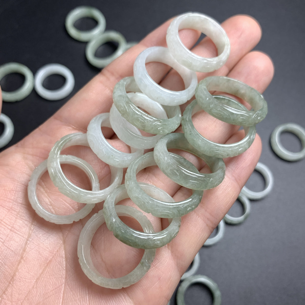 Handful of icy pale green jadeite carved rings showing natural color variation