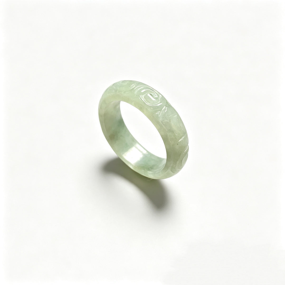 Icy pale green jadeite carved ring on white background with polished interior
