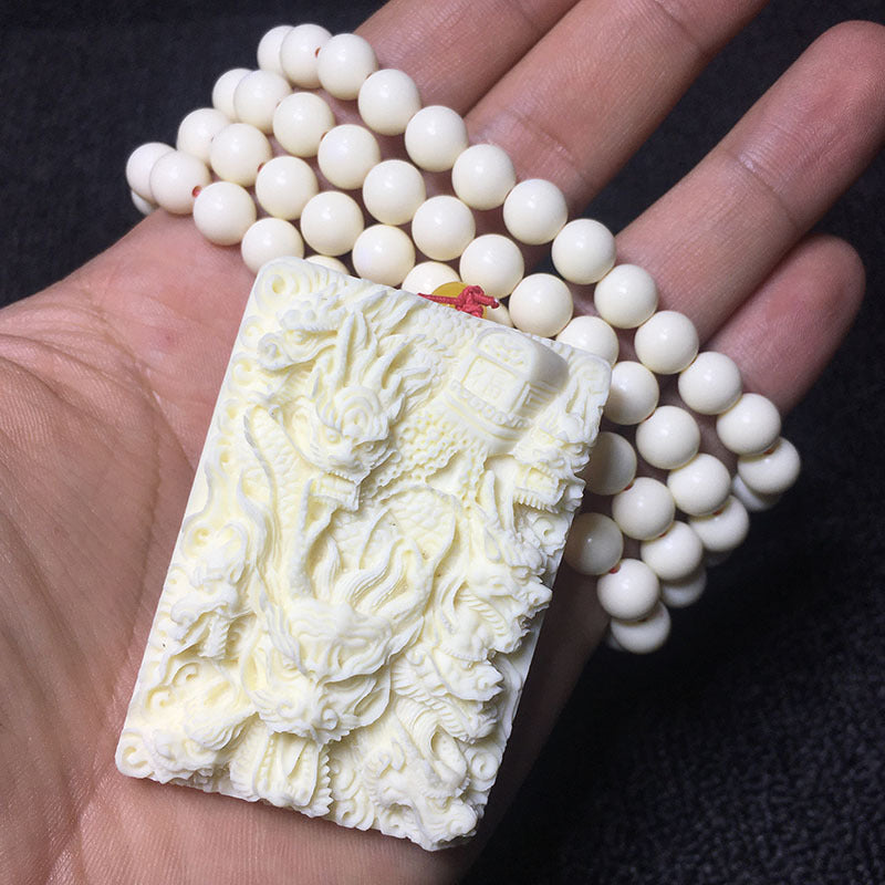 Ivory nut multi-dragon pendant shown in hand with ivory-tone bead strand
