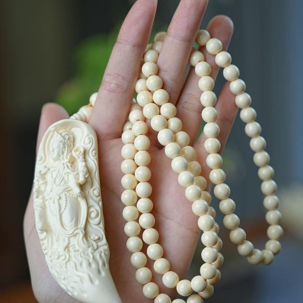 Ivory nut Samantabhadra crescent pendant shown in hand with pale round bead strand for scale