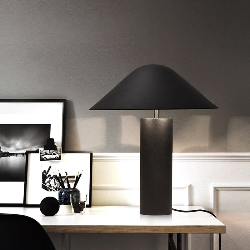 Matte black cone shade table lamp with cylindrical base on desk