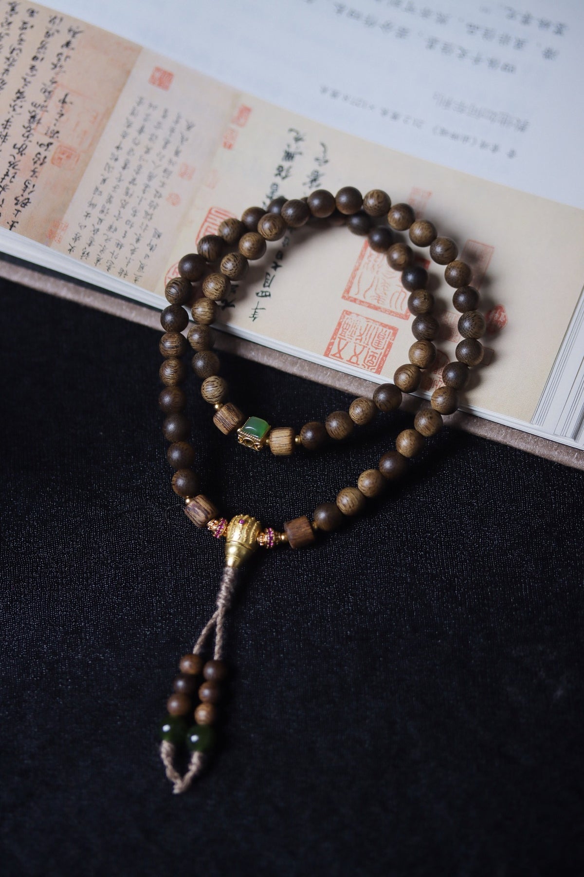 Natural agarwood prayer bead strand with green-tone focal accents, gold-tone detailing and tassel