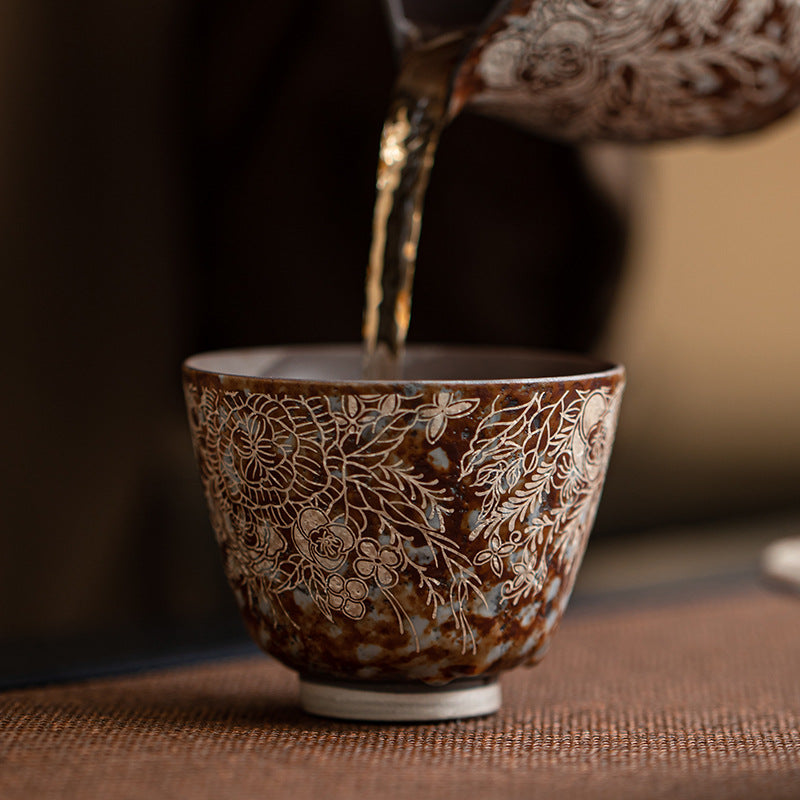 Tea pouring into floral silver-accent rustic ceramic Gongfu cup