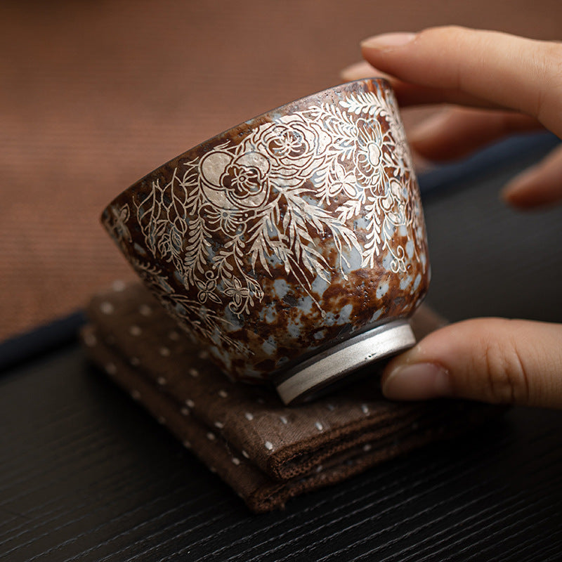 Close-up of floral silver-accent detailing on rustic brown ceramic tea cup