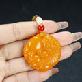 Golden orange round Pixiu wish-fulfillment pendant held in hand