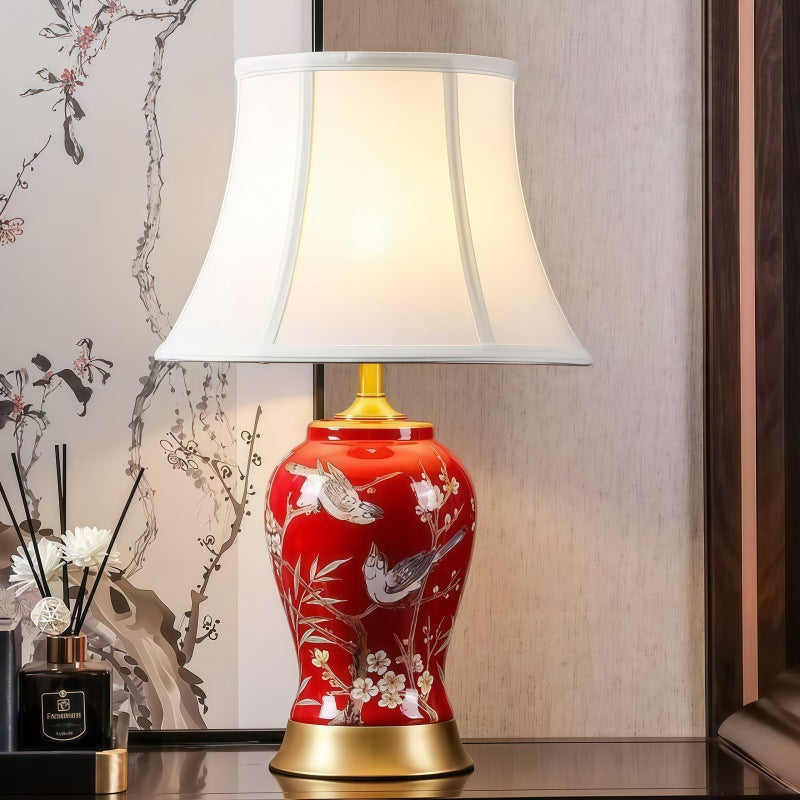 Red porcelain bird and blossom table lamp glowing in bedroom setting