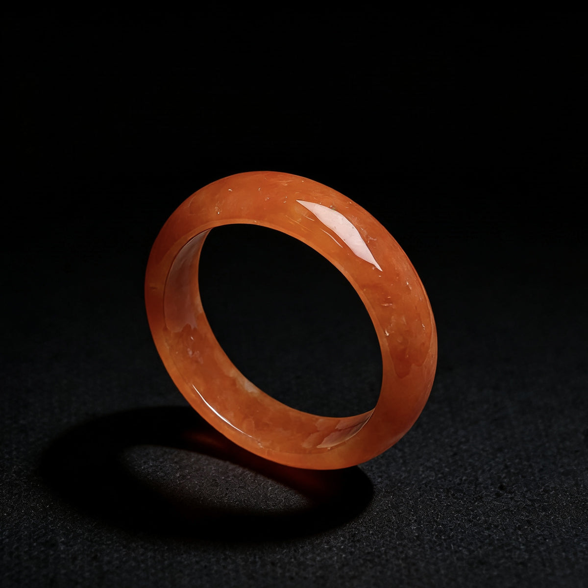 Polished red orange jadeite ring on black background with luminous warm tone
