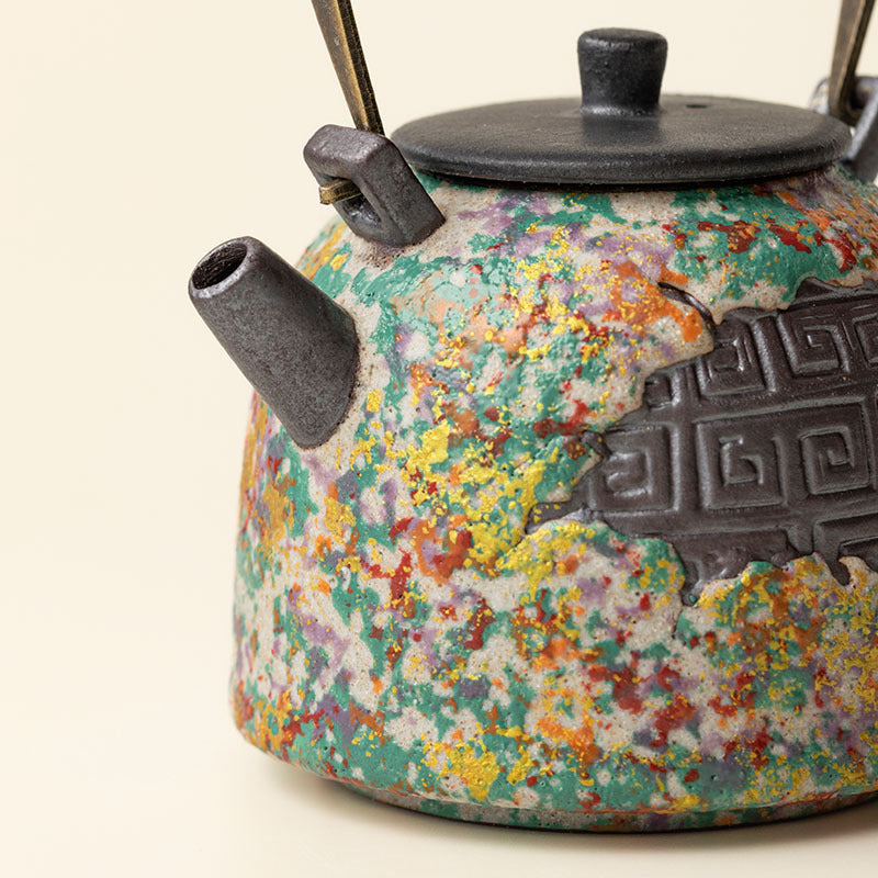 Close-up of multicolor rock-painting glaze and dark meander relief on ceramic teapot