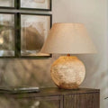 Round stone-finish ceramic table lamp with warm linen shade in neutral interior