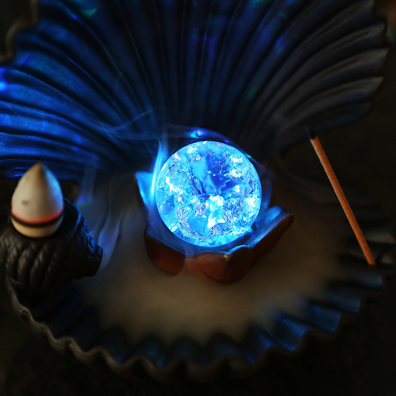 Illuminated blue crystal orb inside shell-shaped incense burner with smoke