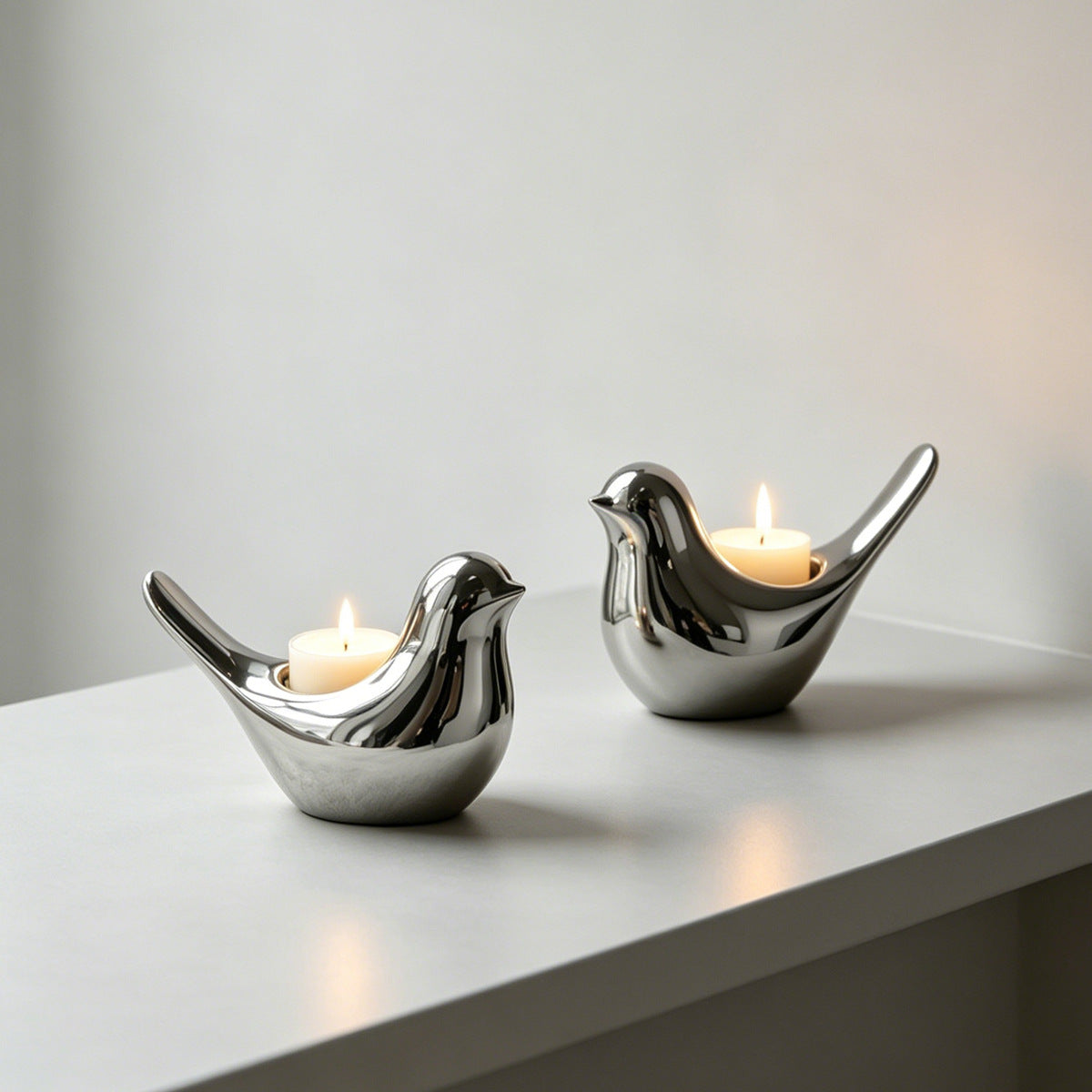Pair of polished silver ceramic bird candle holders with candles