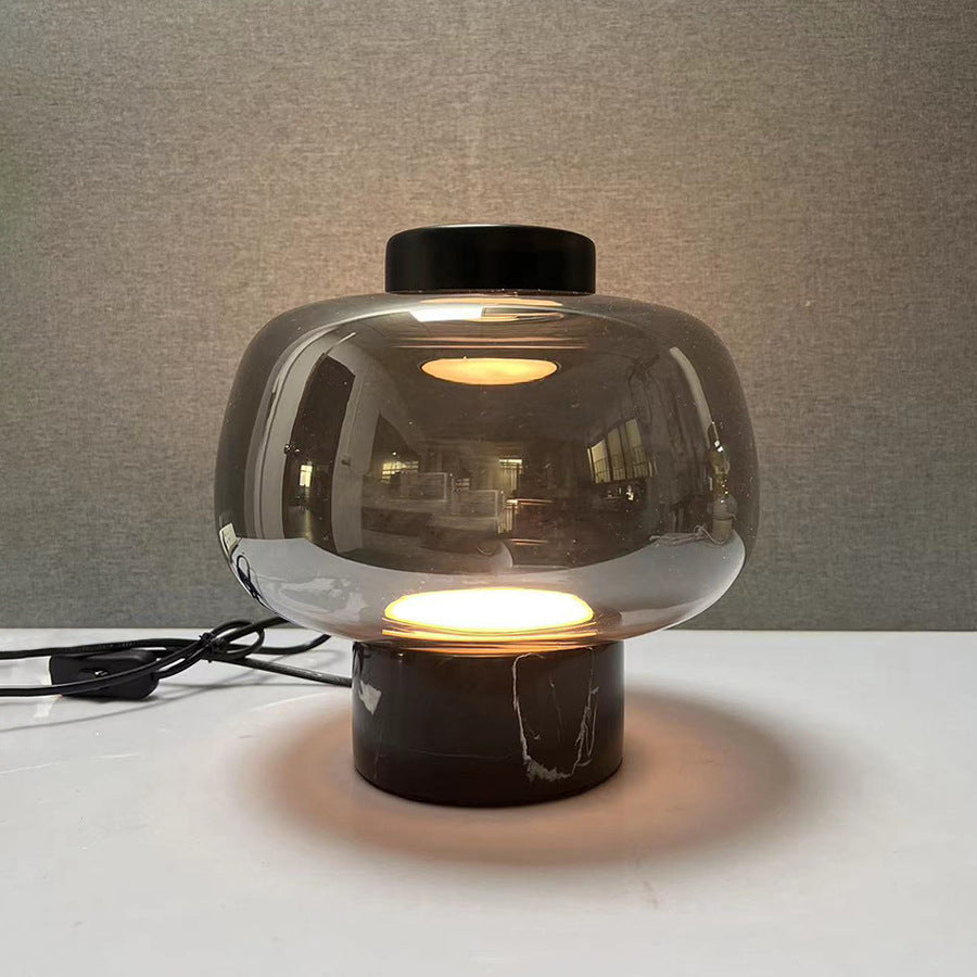Smoke grey glass globe table lamp with black marble base glowing warmly