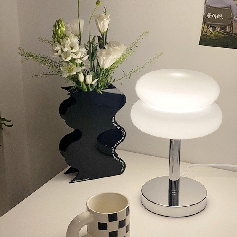 White stacked glass cake table lamp glowing beside sculptural decor