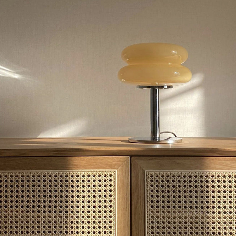 Milk yellow stacked glass cake lamp glowing on a wood cabinet