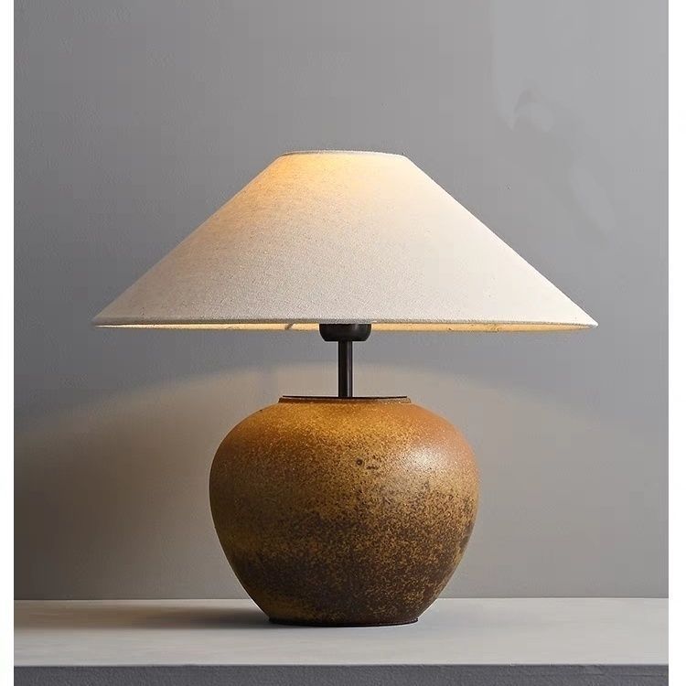 Aged brown round ceramic lamp with conical linen shade on neutral background