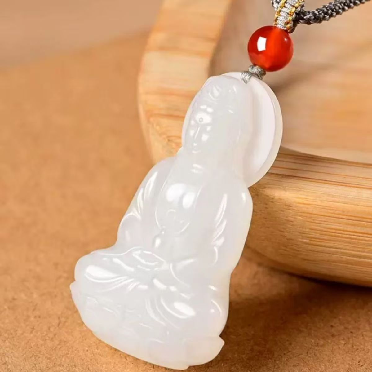 Side view of white Guanyin pendant carving with red accent bead