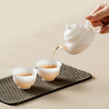 White porcelain Chinese teapot pouring tea into two cups