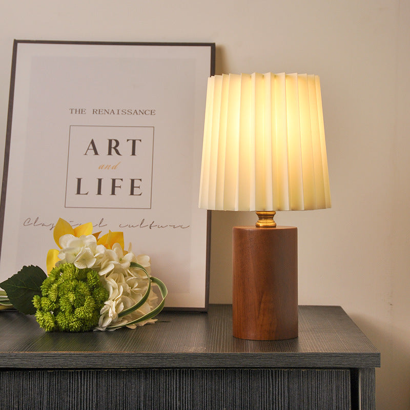 Walnut cylinder table lamp with pleated ivory shade glowing on console