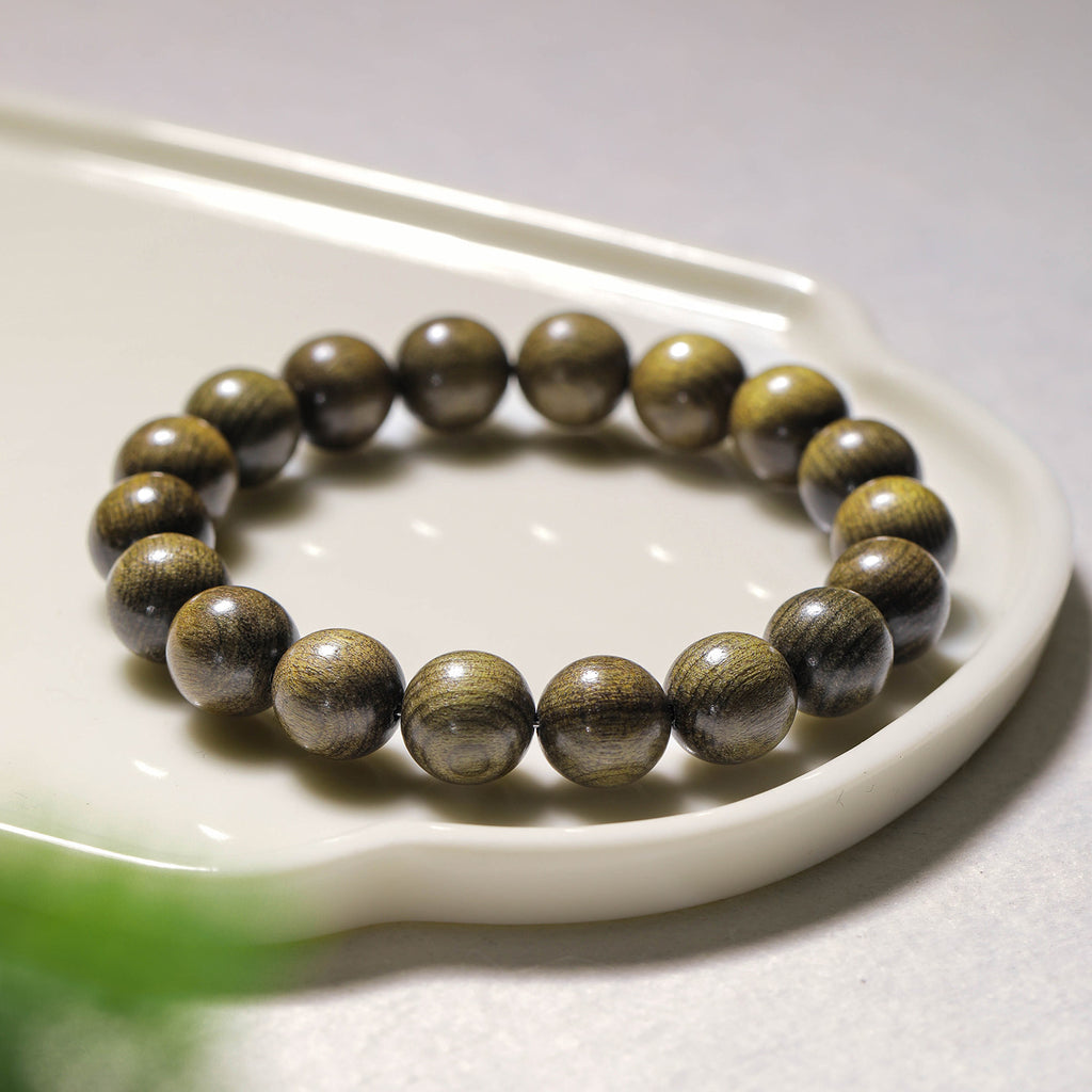 Golden-thread wood bracelet on a ceramic tray showing flowing chatoyant grain