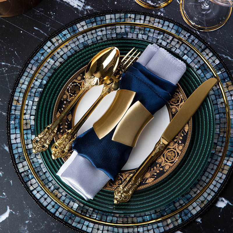 Emerald green and gold table setting with layered plates on a round shell mosaic placemat