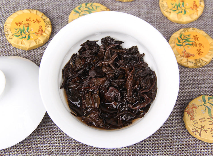 Brewed Huangjing ripe Pu-erh leaves in a white gaiwan with wrapped mini cakes