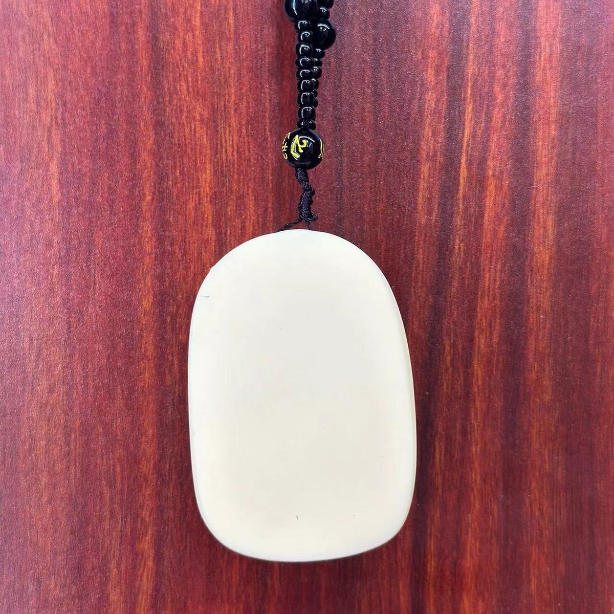Back view of ivory nut Manjushri Bodhisattva pendant with black bead cord, smooth tagua vegetable ivory reverse