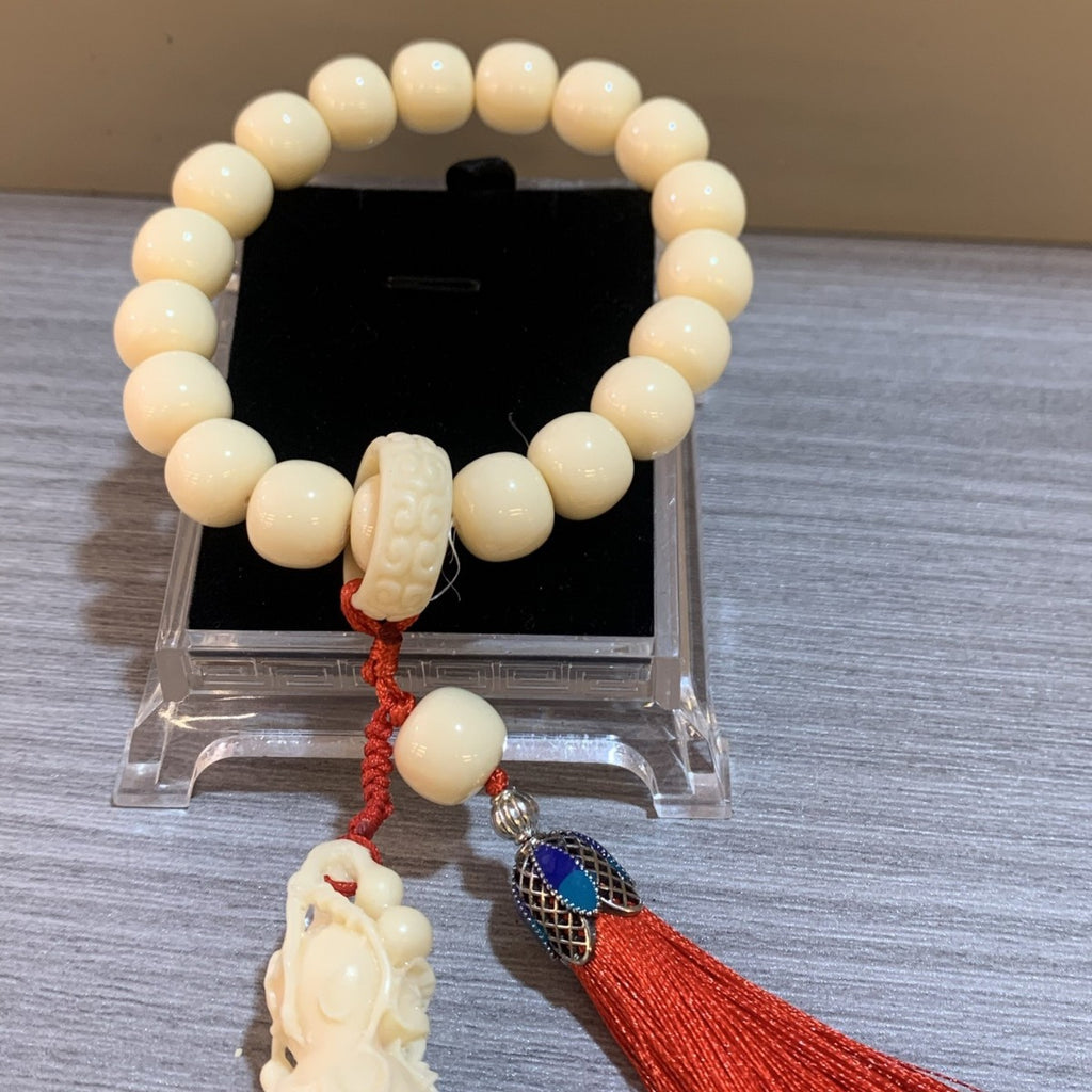 Close-up ivory nut vegetable ivory bead bracelet with carved centerpiece and red tassel charm