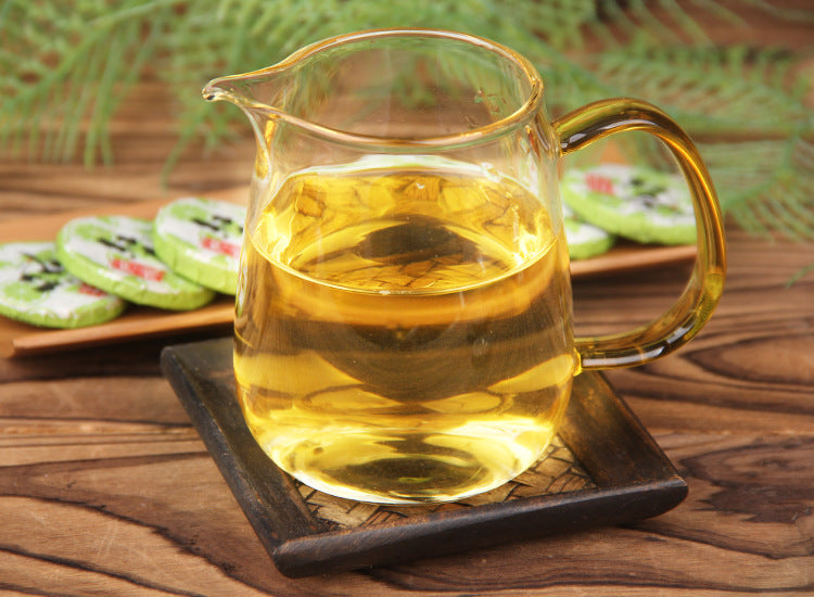 Glass pitcher of brewed lemon Dianhong black tea with wrapped mini cakes in background