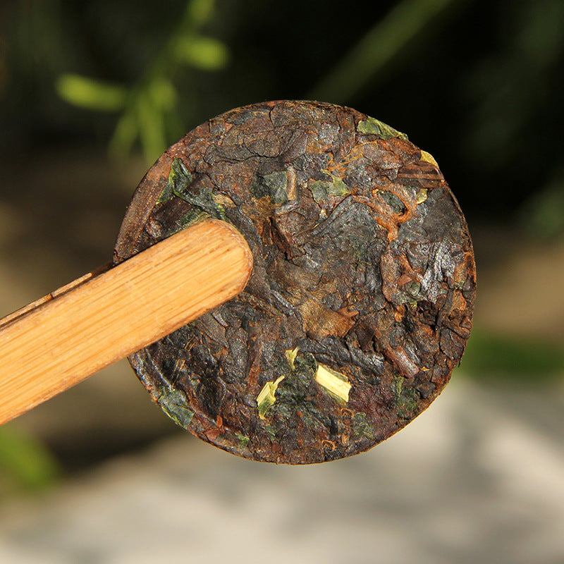 Unwrapped sticky rice aroma ripe Pu-erh mini cake with visible nuo mi xiang leaves