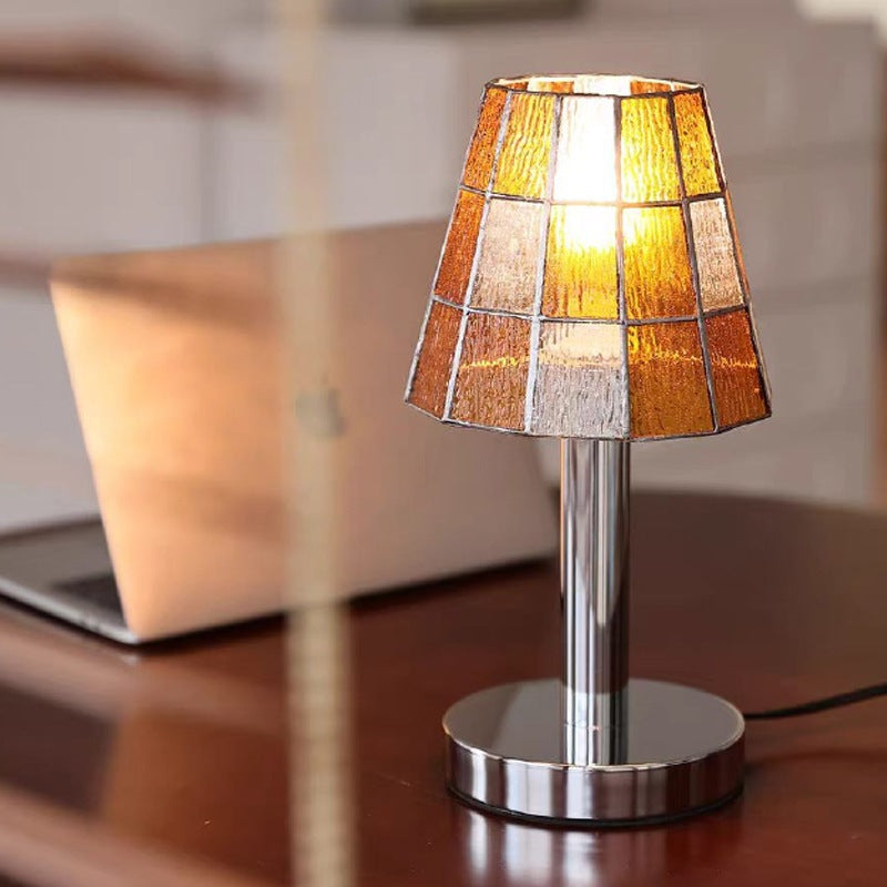 Orange mosaic stained glass lamp glowing warmly beside a laptop