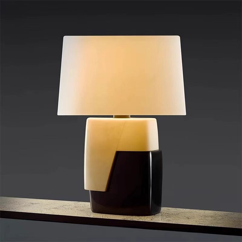 Black and ivory designer table lamp glowing warmly against dark background