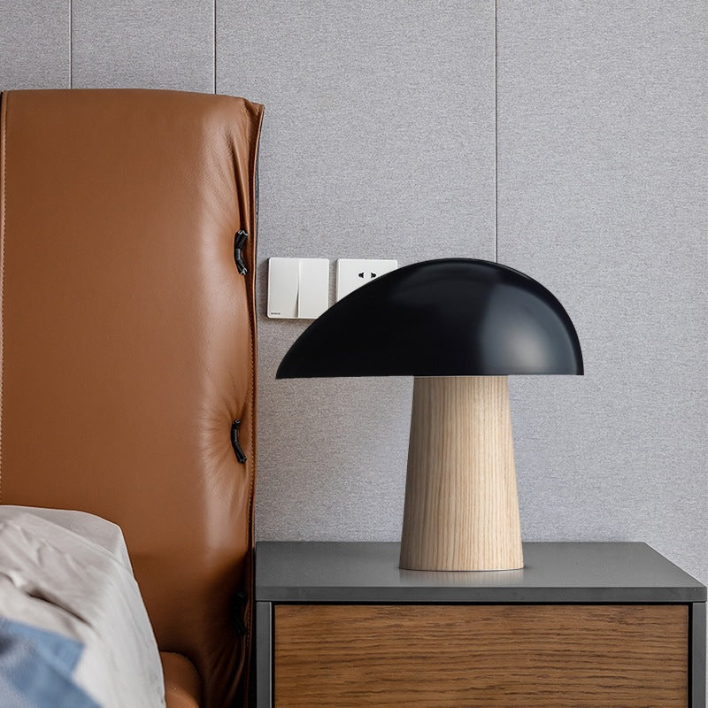 Black mushroom table lamp with natural wood-look tapered base on a bedside cabinet