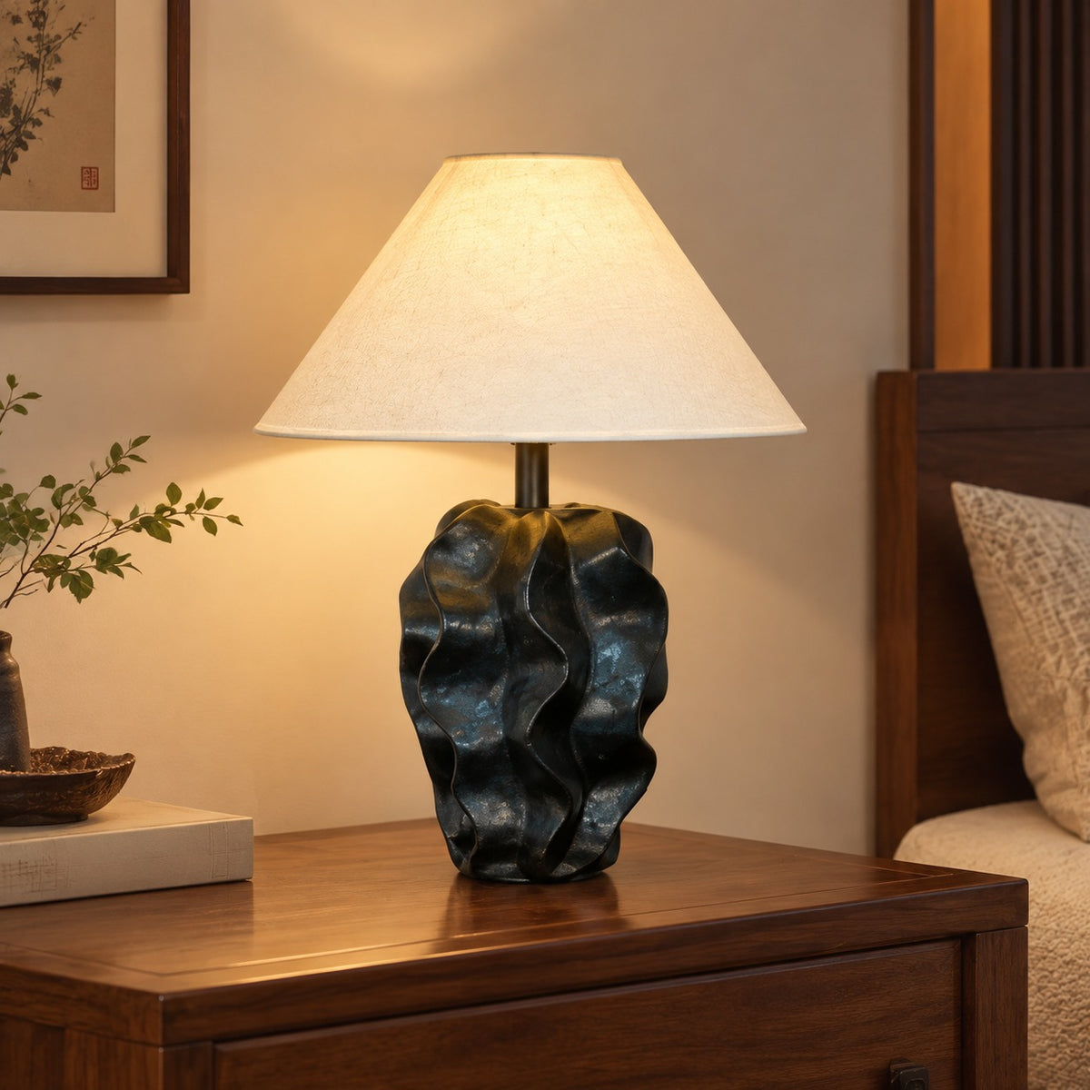 Black sculptural ceramic rock-form table lamp with warm linen shade in a wood bedroom