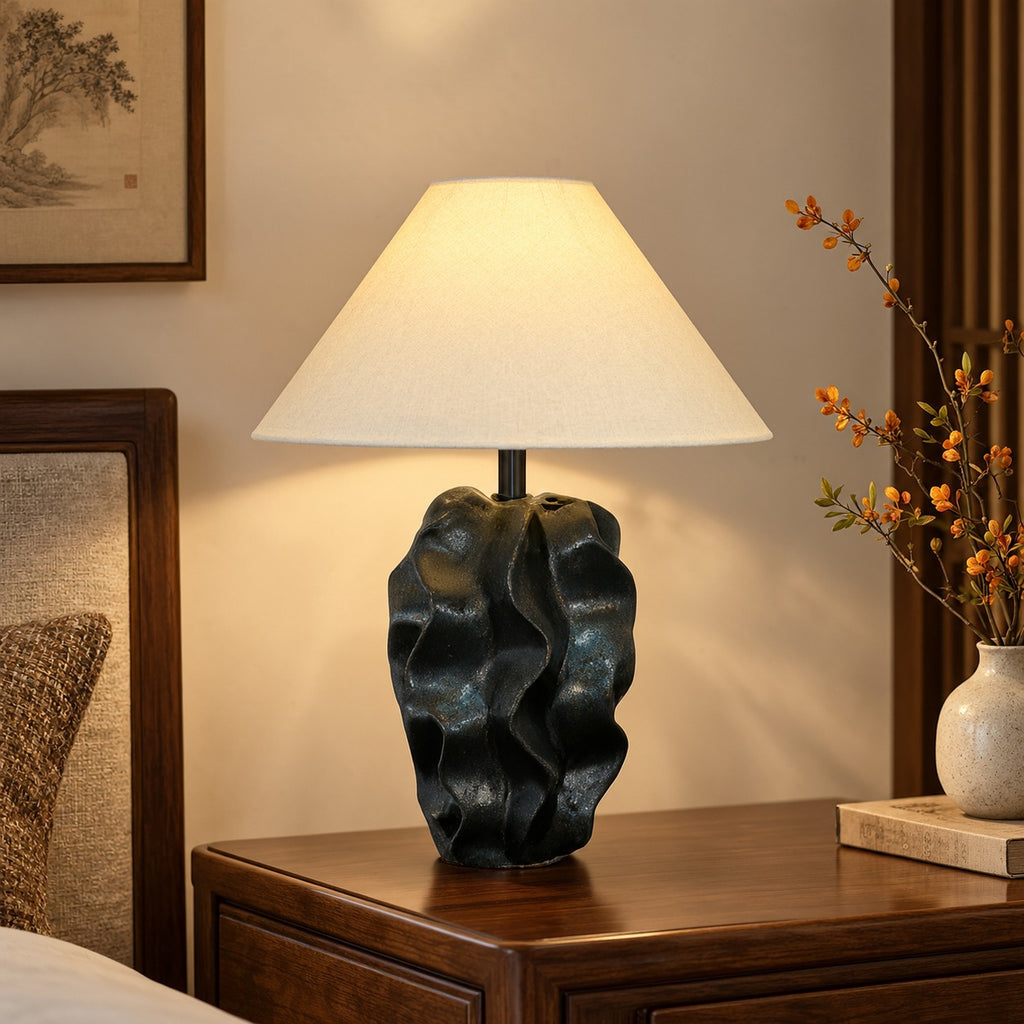 Black sculptural wabi-sabi table lamp styled beside woven and wood furniture