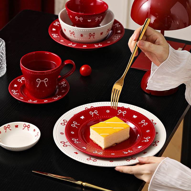 Red and ivory bow ceramic tableware styled on a black dining table with cake and gold flatware