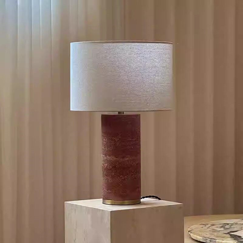 Tall red travertine column table lamp with drum shade in a warm bedroom