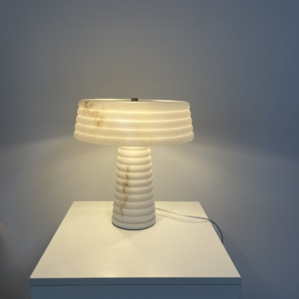 Layered white faux marble resin table lamp with ribbed shade and column glowing warmly