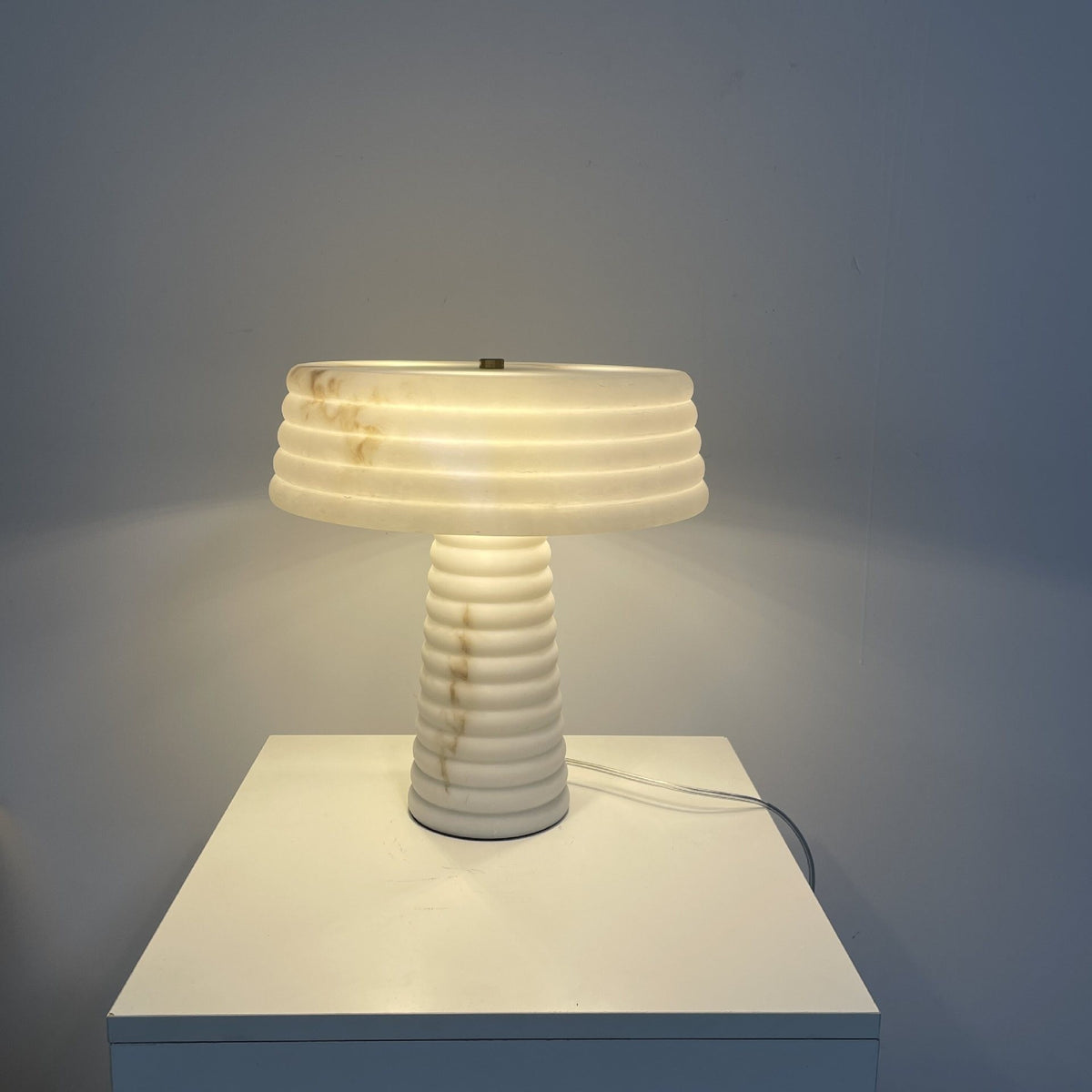 Layered white faux marble resin table lamp with ribbed shade and column glowing warmly