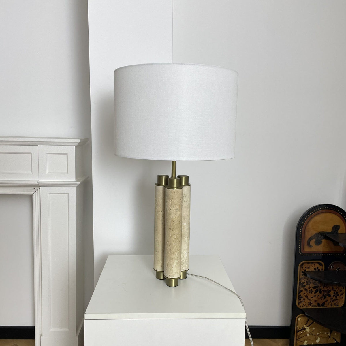 Natural travertine and brass column table lamp with white drum shade in a modern interior