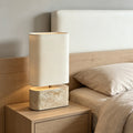 Yellow travertine oval base table lamp with tall ivory fabric shade beside a bed